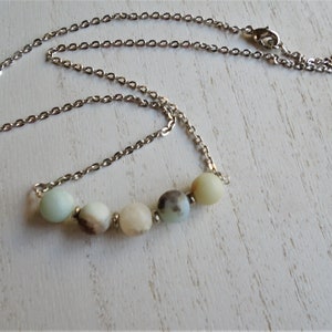 Puede incluir: Un collar de cadena plateada con una fila de cinco cuentas redondas de color verde claro, blanco y marr&oacute;n.