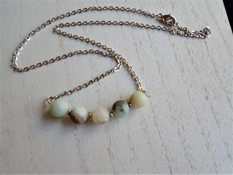 Puede incluir: Un collar de cadena plateada con una fila de cinco cuentas redondas de color verde claro, blanco y marr&oacute;n.