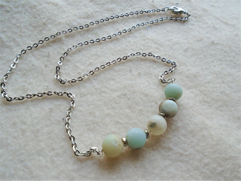 Puede incluir: Un collar de cadena plateada con una fila graduada de cinco cuentas redondas de color verde claro y blanco.