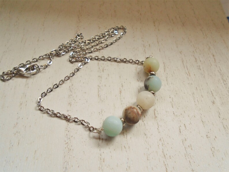 Puede incluir: Un collar de cadena de plata con una fila de seis cuentas redondas de color azul claro y marr&oacute;n.