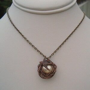 May include: A bronze chain necklace with a pendant featuring a bird in a wire nest with a pearl in the center.