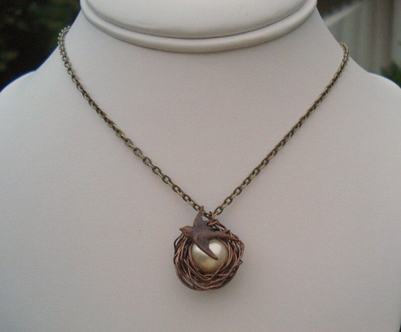 May include: A bronze chain necklace with a pendant featuring a bird in a wire nest with a pearl in the center.