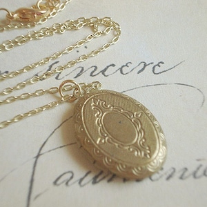 May include: A gold chain necklace with a gold oval locket. The locket has a detailed engraved design.