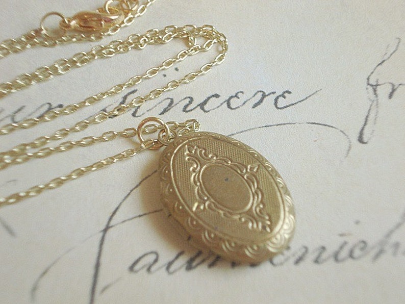 May include: A gold chain necklace with a gold oval locket. The locket has a detailed engraved design.