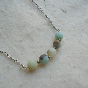 Puede incluir: Un collar de cadena plateada con una fila de cinco cuentas de piedras preciosas de color verde claro y blanco.