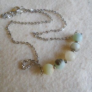 Puede incluir: Un collar de cadena de plata con un colgante de cinco piedras redondas de color verde claro y blanco.