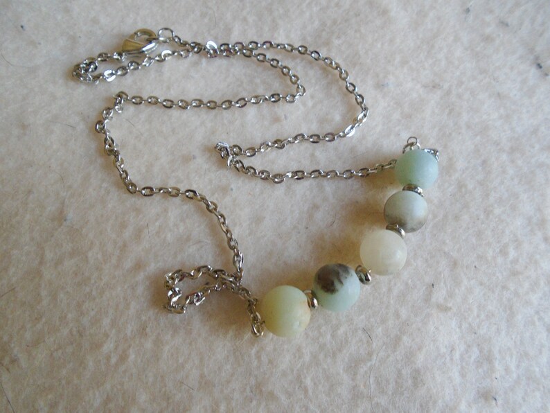 Puede incluir: Un collar de cadena de plata con un colgante de cinco piedras redondas de color verde claro y blanco.
