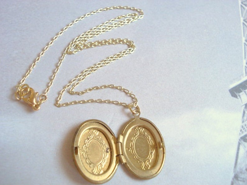 May include: A gold chain necklace with an oval locket pendant. The locket is open, revealing two empty compartments.