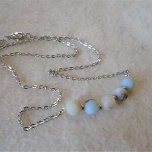 Puede incluir: Un collar de cadena de plata con una fila de cuentas redondas de color azul claro y blanco.
