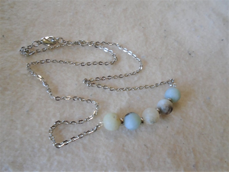 Puede incluir: Un collar de cadena de plata con una fila de cuentas redondas de color azul claro y blanco.