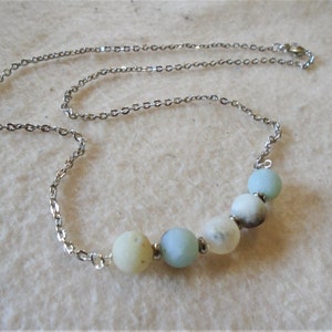 Puede incluir: Un collar de cadena plateada con una fila de cuentas redondas de color azul claro y blanco.