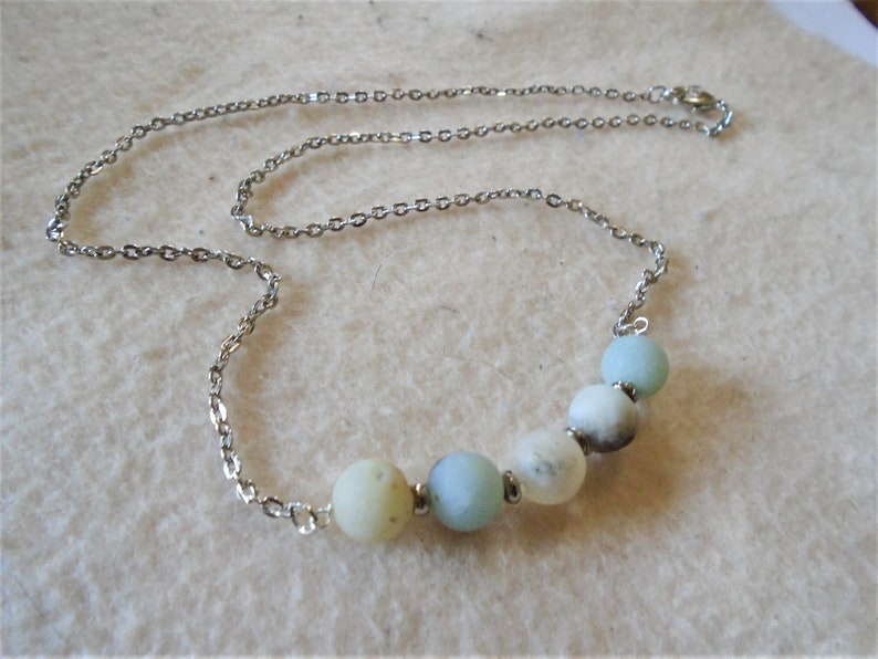 Puede incluir: Un collar de cadena plateada con una fila de cuentas redondas de color azul claro y blanco.