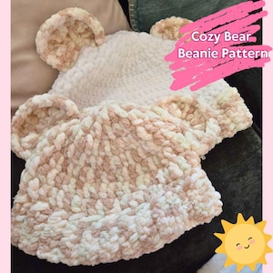 May include: A cosy bear beanie knitting pattern featuring two crocheted beanies in white and cream with brown ear accents. The text "Cozy Bear Beanie Pattern" is written in pink on a white background.