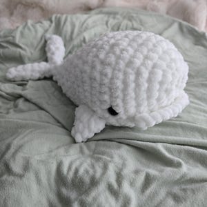 May include: A white crocheted whale plush toy with black eyes, lying on a light green blanket.