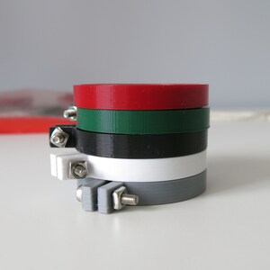 May include: A set of five embroidery hoops in different colours, including red, green, black, white, and grey. The hoops are stacked on top of each other, with the largest hoop at the bottom and the smallest hoop at the top.