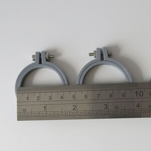 May include: Two grey embroidery hoops with a silver screw on each hoop. The hoops are measured with a ruler that shows inches and fractions of an inch. The smaller hoop measures 4 inches in diameter and the larger hoop measures 6 inches in diameter.