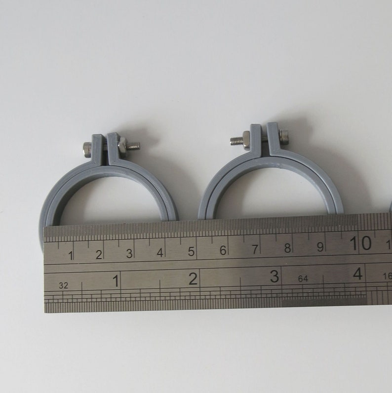 May include: Two grey embroidery hoops with a silver screw on each hoop. The hoops are measured with a ruler that shows inches and fractions of an inch. The smaller hoop measures 4 inches in diameter and the larger hoop measures 6 inches in diameter.