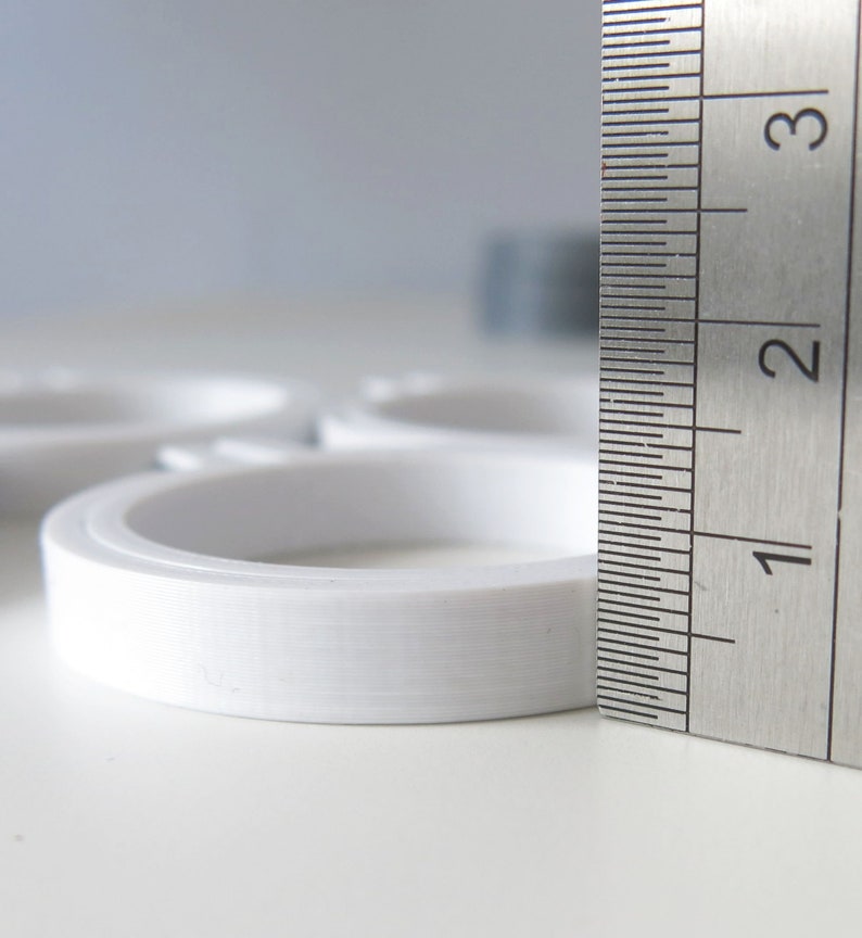 May include: A white plastic ring measuring 2.5 cm in diameter, next to a metal ruler marked with centimetres.
