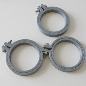 May include: Three grey embroidery hoops of different sizes. The hoops are made of plastic and have a screw-on closure.