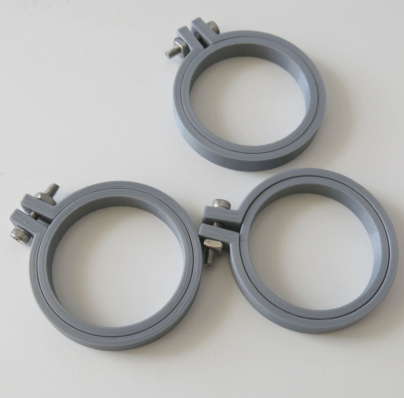May include: Three grey embroidery hoops of different sizes. The hoops are made of plastic and have a screw-on closure.