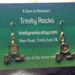 Puede incluir: Pendientes de oro con una pequeña piedra redonda y transparente en el centro. Los pendientes tienen forma de tres puntas, cada una de las cuales se asemeja a una pala. Los pendientes se muestran en una tarjeta con el texto "A Gem to Discover! Trinity Rocks trinityrocks.etsy.com Main Road, Trinity East, NL".