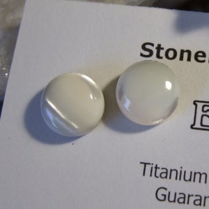 May include: Two white pearl ear studs on a white card with the text "Stonebeads by Chris" and "Earstuds". The card also states "Titanium Ear Posts & Clutches Guaranteed Hypo-Allergenic".