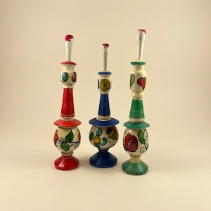 May include: Three hand-painted wooden decorative objects. Each has a unique color scheme, including red, blue, and green, with floral and heart designs. The objects have a layered design with a rounded base and a top with a red or white accent.