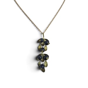 Op de afbeelding: Een ketting met een hanger in de vorm van een tros donkerblauwe bessen met gestructureerde koperen bladeren en stengels. De hanger hangt aan een dunne, verfijnde goudkleurige metalen ketting. Het ontwerp bootst een botanische tak met bessen na.