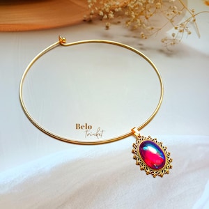 May include: A gold choker necklace with a pendant. The pendant features an oval iridescent stone in pink, blue, and purple, set within a detailed gold frame. The text "Belo Trinket" is visible. A stylish piece of jewellery.