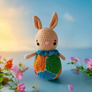 May include: A crocheted bunny toy with a pink nose and black eyes. The bunny is wearing a colorful patchwork dress with orange, green, blue, and yellow squares.