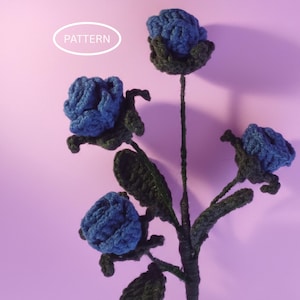 Op de afbeelding: Een handgemaakte gehaakte bloemstengel met vier blauwe bloemen en donkergroene bladeren. Het woord "PATTERN" staat in een witte ovaal. De achtergrond is lichtpaars.