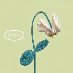 May include: A crocheted flower with off-white petals, a small yellow center, and two textured teal leaves on a long, thin teal stem. The stem curves at the top to support the flower head. The word PATTERN is printed in white inside an oval.