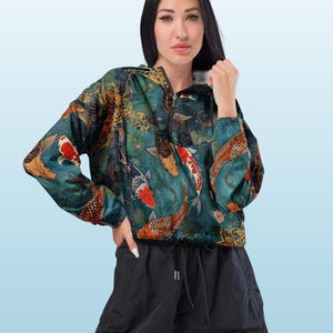 May include: A long-sleeve, quarter-zip hooded jacket featuring a vibrant all-over print of orange, white, and black koi fish swimming amidst dark teal water and aquatic plants. The jacket includes a drawstring hood and a black drawstring hem.