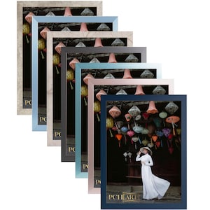 Op de afbeelding: Een set van acht fotolijsten in verschillende kleuren, waaronder zilver, lichtblauw, beige, donkergrijs, lichtblauw, roze en donkerblauw. De lijsten zijn in een stapel gerangschikt, met de grootste lijst onderaan en de kleinste lijst bovenaan. De lijsten zijn allemaal van hout en hebben een eenvoudig, modern ontwerp. De grootste lijst bevat een foto van een vrouw in een witte jurk die voor een gebouw staat met kleurrijke lantaarns die aan het plafond hangen. De tekst "PCHEART" is in goud op de onderkant van de lijst gedrukt.
