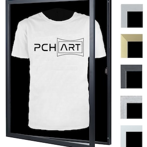 Könnte beinhalten: Ein schwarzer Schattenkastenrahmen mit einem weißen T-Shirt darin. Das T-Shirt trägt den Aufdruck "PCH ART". Der Rahmen hat einen schwarzen Passepartout und eine transparente Acrylglasscheibe.