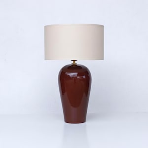 Può includere: Una lampada da tavolo con una base in ceramica rosso scuro lucido e un paralume color crema. La lampada ha un design classico ed elegante, adatta per un soggiorno o una camera da letto. La base è alta circa 46 cm.