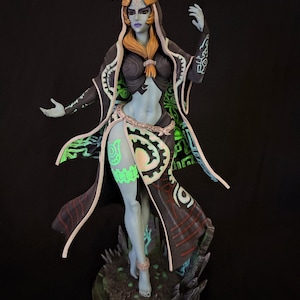 May include: A standing figurine of a pale blue-skinned character with long blonde hair, wearing a dark hooded cloak with white trim and glowing green geometric patterns. The figure features intricate markings on the skin and stands on a dark base.