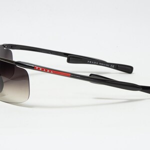 May include: Black Prada sunglasses with gradient lenses. The temples are black with the Prada logo in red and white. The sunglasses are made in Italy.