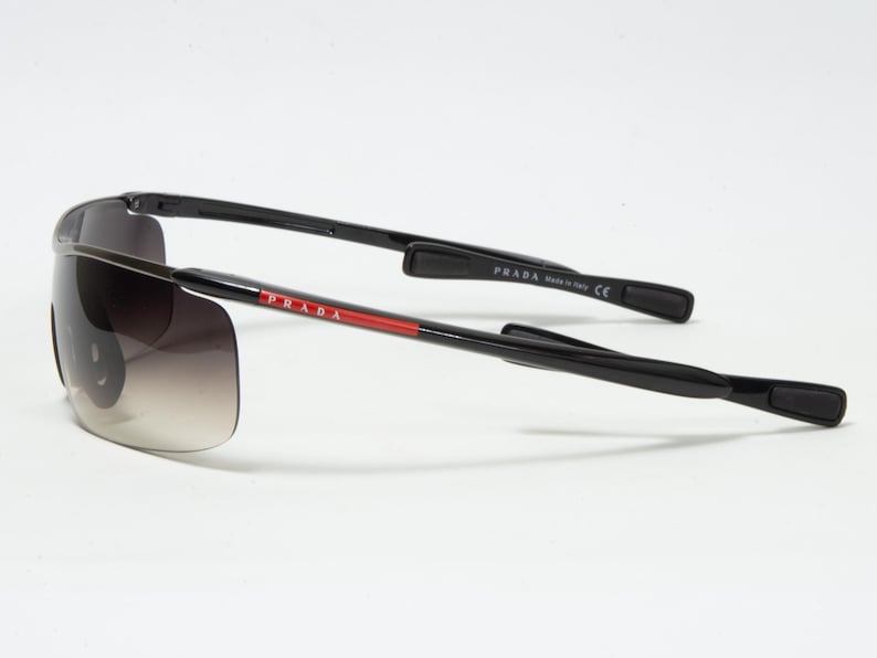 May include: Black Prada sunglasses with gradient lenses. The temples are black with the Prada logo in red and white. The sunglasses are made in Italy.