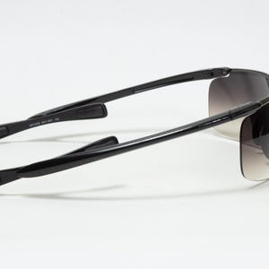 May include: Black sunglasses with a wraparound design. The lenses have a gradient tint, transitioning from dark at the top to lighter at the bottom. The arms are sleek and black, with a curved design for a comfortable fit.