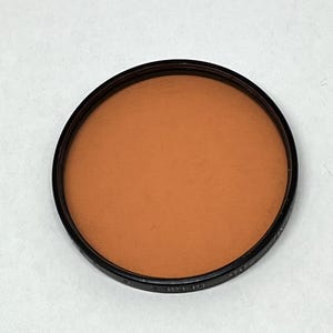 May include: A round, orange-coloured filter for a camera lens. The filter is in a black plastic frame.