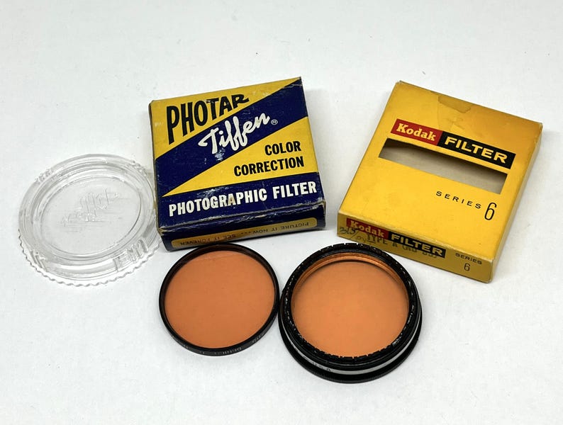 May include: Two orange photographic filters, one in a blue box labelled "Photar Tiffen Colour Correction Photographic Filter" and the other in a yellow box labelled "Kodak Filter Series 6".