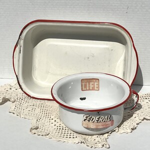 May include: Two vintage white enamelware kitchen items with red trim. A rectangular baking dish and a round bowl with a handle. The bowl has the text "ADVERTISED IN LIFE" and "FEDERAL ENAMELED WARE" on it.