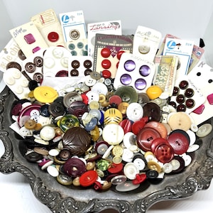 May include: A large collection of assorted buttons in various shapes, sizes, and colors, including red, white, yellow, brown, and purple, piled inside an ornate silver-toned metal tray, with several original cardboard retail display cards.