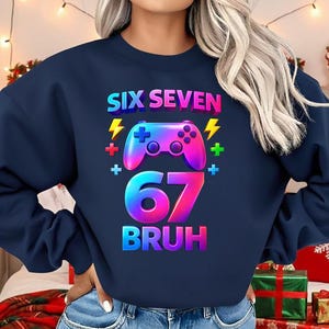 Może przedstawiać: Granatowa bluza z kolorową grafiką z napisem "SIX SEVEN" nad obrazem kontrolera, liczbą "67" i słowem "BRUH". Projekt zawiera błyskawice i znaki plus. Bluza jest noszona z niebieskimi szortami dżinsowymi.
