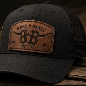 May include: A black baseball cap with a mesh back and a brown leather patch on the front. The patch features the text B BAR B RANCH, the letters BB with long horns, two small stars, and the text EST. 1978 embossed in a dark brown color.