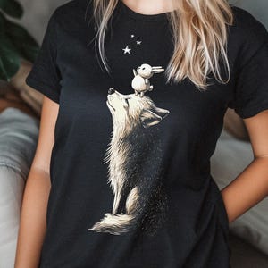 May include: Black t-shirt featuring a graphic of a wolf howling at the stars with a rabbit on its head.