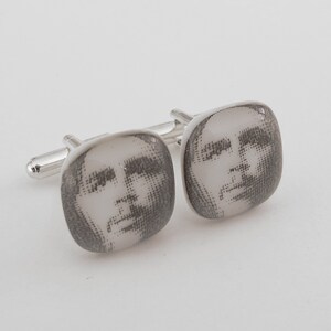 May include: A pair of silver cufflinks with a black and white portrait of a man's face on each cufflink.