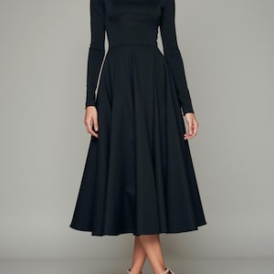 May include: A black midi dress with long sleeves and a boat neckline. The dress has a fitted bodice and a full skirt.