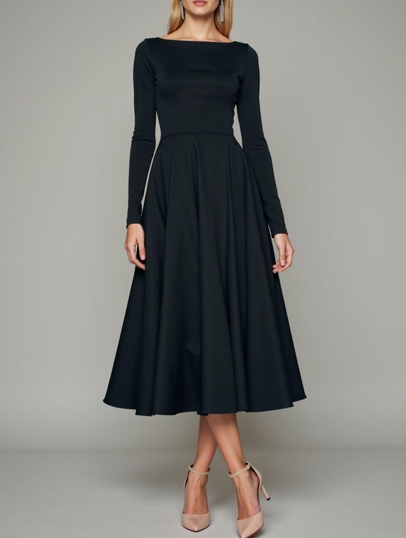 May include: A black midi dress with long sleeves and a boat neckline. The dress has a fitted bodice and a full skirt.